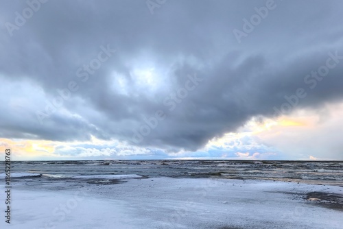 Bilde på lerret Heavy storm clouds roll across the sky as restless waves move beneath glowing sunset light, creating a powerful, moody seascape filled with tension and atmosphere