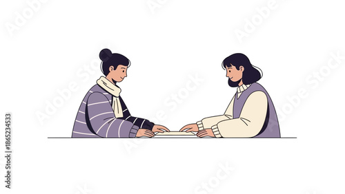 Two women sitting at a table, collaborating on a document or book.