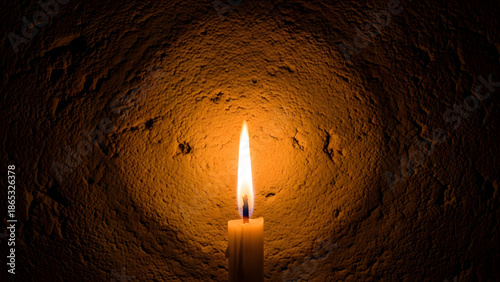 A single candle illuminates a textured wall, casting a warm and comforting glow in the darkness
