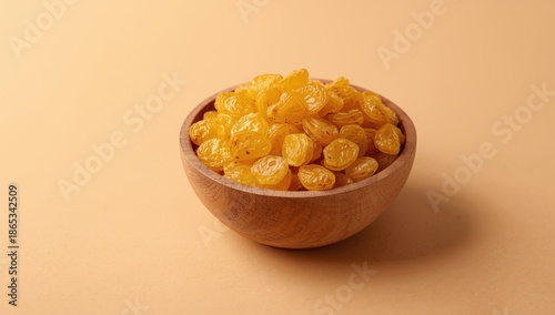 Yellow sultana raisins displayed in a wooden bowl on a beige surface as a food photography backdrop