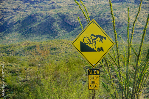 A sign in Saguaro National Park, Arizona against a background of mountains warns bicyclists of a dangerous, steep hill ahead.