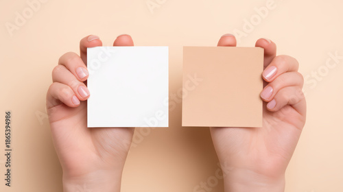 Minimal style close up of hands holding two square paper sheets in white and beige colors on soft peach background, showing contrast and simplicity in design and color tones