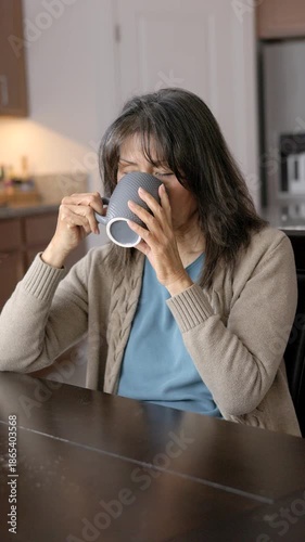 Business woman working at home taking break drinking morning coffee sitting at kitchen table looking out window vertical video