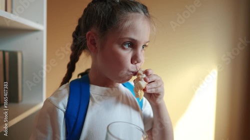 schoolgirl eats a sandwich drinking juice at school during recess with backpack and education bookcase. child lunch concept. indoor child in classroom having lunch snack with bread and sandwich