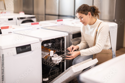 Fotografie Young woman buyer chooses electric dishwasher in home appliance store