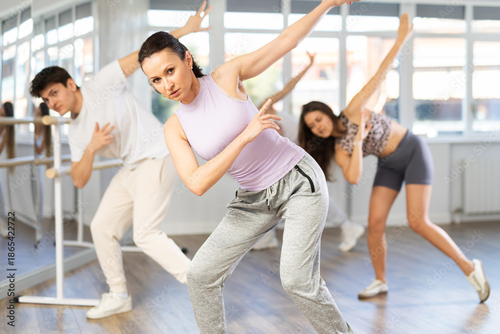 Obraz premium Expressive woman in casual tank top and sweatpants honing hip-hop dance moves in choreographic studio setting during group training