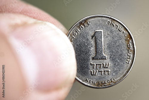 Tableau sur toile Macro close-up of an old rusty used Israeli one shekel coin held between fingers, showing metal texture, denomination, and national currency detail