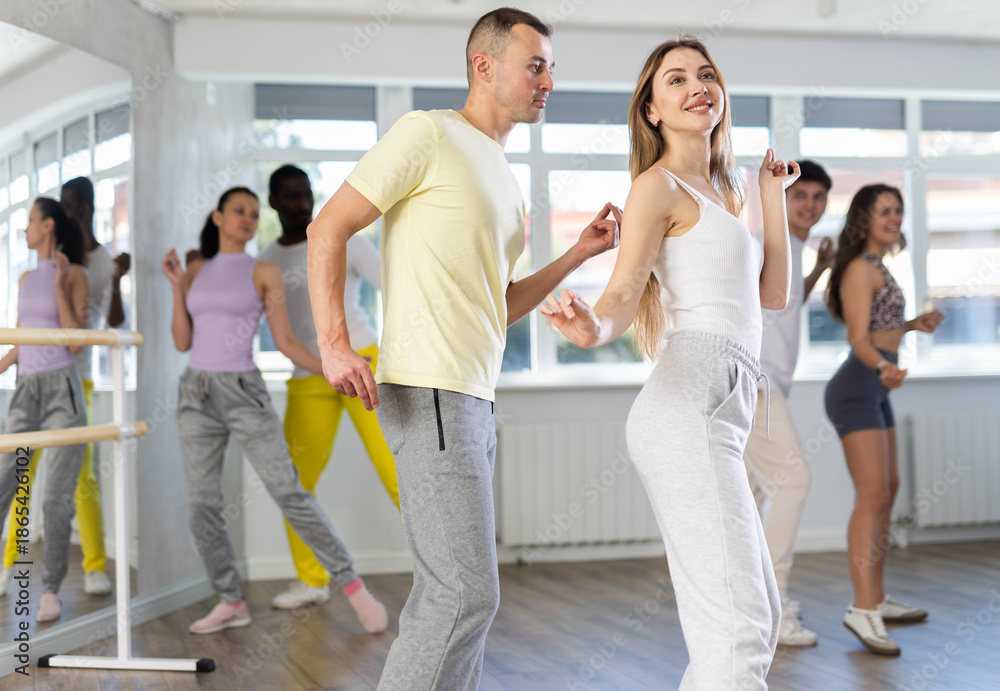 Naklejka premium Happy young woman and man with group of multinational people enjoying active boogie-woogie dance in modern studio. Social dancing concept