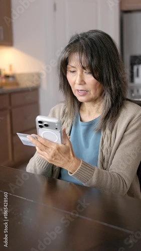 Woman enjoying shopping online holding credit card using smartphone relaxing sitting at kitchen table vertical video