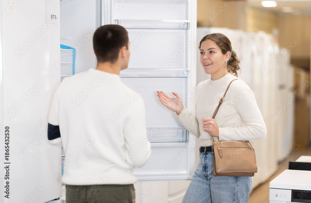 Fototapeta premium Young couple chooses modern fridge at a hypermarket