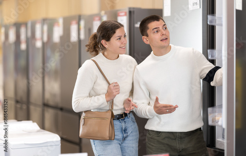 Foto Young couple together choose a large refrigerator for the kitchen in a new apartment