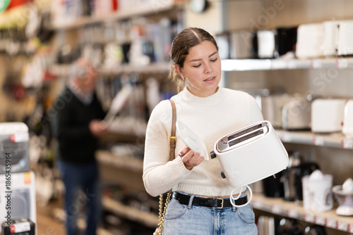 Bild auf Leinwand Young woman buyer chooses electric toaster in home appliance store