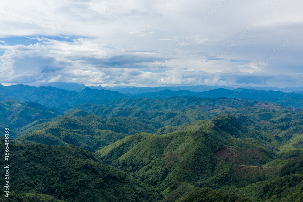 Obraz premium Sweeping panorama of undulating green hills and distant blue ridges beneath a vast sky filled with layered clouds in the Laotian countryside between Phonsavan and Phou Khoun. The landscape showcases