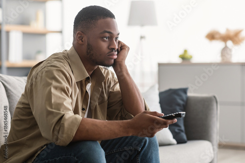 Canvas Print Bored African American Man Watching Boring TV Switching Channels Holding Television Remote Controller Sitting On Sofa At Home