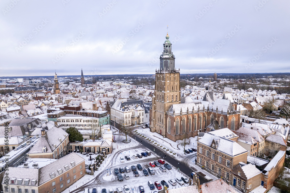 Fototapeta premium Medieval Hanseatic Dutch tower town Zutphen in the Netherlands covered in snow with historic heritage buildings and river IJssel passing by in the background behind Walburgiskerk church tower