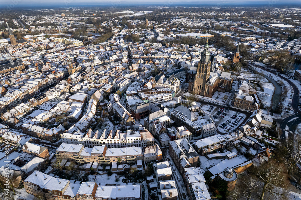 Obraz premium Medieval Hanseatic Dutch tower town Zutphen in the Netherlands covered in snow with historic heritage buildings and river IJssel passing by in the background behind Walburgiskerk church tower