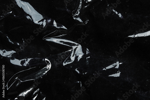 Photos Black glossy wrinkled plastic texture with light reflection, abstract background