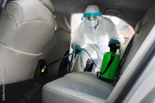 Fotografi Worker in hazmat suit with chemical alcohol spray cleaning inside car to disinfect and decontaminate covid-19 by specialist cleaner wearing personal protective equipment PPE