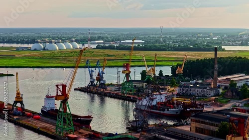 Wallpaper Mural Industrial port scene with cargo ships, cranes, storage domes, and evening light creating a dynamic maritime atmosphere ideal for logistics, industry, and infrastructure projects. Torontodigital.ca