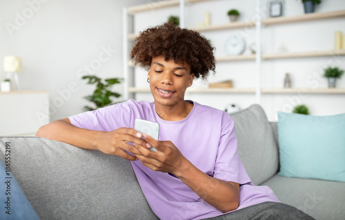 Canvas Print Cool black teenager with mobile phone studying online, chatting with friend, posting in social media from home