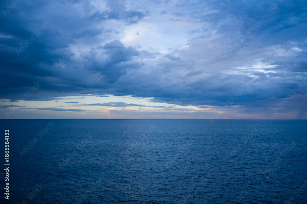 Obraz premium Vast expanse of the Adriatic Sea stretches to the horizon beneath a sky filled with layered, moody clouds at dusk. The scene captures subtle color gradients and gentle waves, evoking a tranquil and