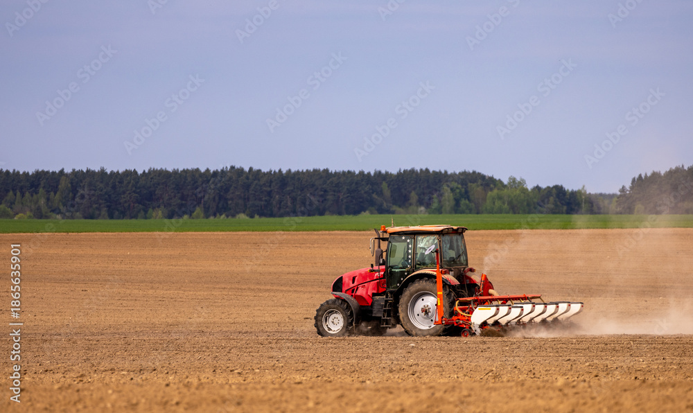 Fototapeta premium Farmer in tractor preparing farmland with seedbed for the next year. Powerful tractor at work, turning over soul on a vast farmland under a clear sky.