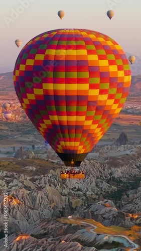 Vertical video. Goreme, Nevsehir, Turkey. Detailed view of large checkered hot air balloon with vibrant color pattern in morning sunlight over Turkish landscape. Aerial View. Rich colors