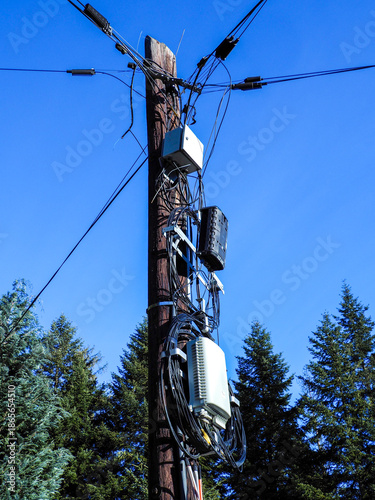 Close up view of wooden telecommunications pole with tangled wires and equipment boxes in mountain area.