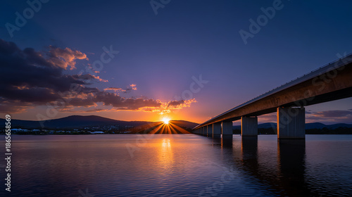 Wallpaper Mural Sunset over a calm lake with a long bridge extending across the water, mountains in the background, and dramatic clouds illuminated by the golden sun Torontodigital.ca