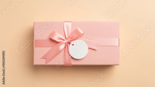 A pink gift box with a ribbon and tag on a beige background