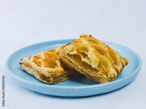 Golden flaky puff pastry cut in half on a blue ceramic plate, showing layered buttery texture, isolated on white background. Minimal bakery food concept with copy space