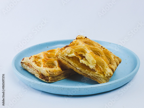 Golden flaky puff pastry cut in half on a blue ceramic plate, showing layered buttery texture, isolated on white background. Minimal bakery food concept with copy space