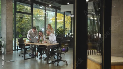 A modern office interior, featuring a blurred view of workers at desks, through a glass partition.
