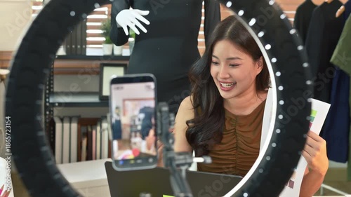 SME business asian woman using laptop and recording video or live streaming for sell fashion dress.