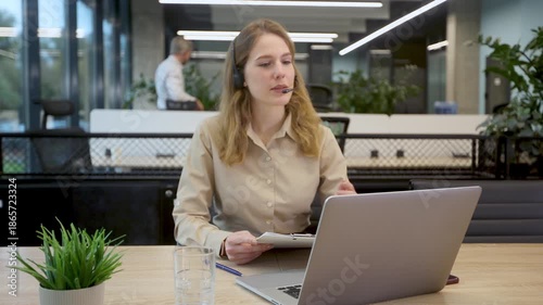 Friendly female helpline operator in call center. Young woman working in call center and holding microphone on headset with hand.