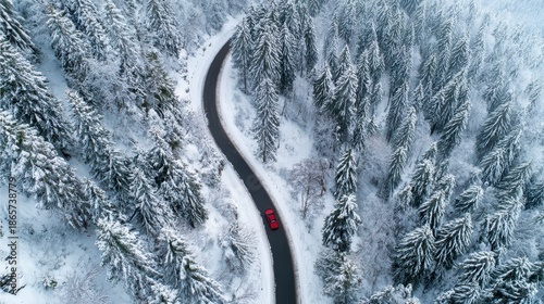 Aerial view of a winding road snaking through a snowy forest, with a red car visible