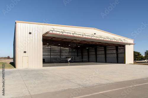 Foto Small jet inside beige metal aircraft hangar on clear sunny day