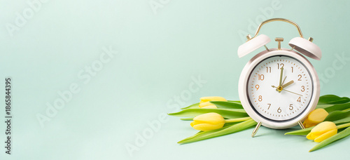 Alarm clock with yellow tulip flowers, switch to daylight saving time in spring, summer time changeover
