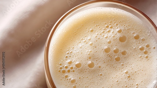 Close-up of a frothy beverage in a glass, showcasing bubbles and creamy texture, resting on a soft fabric surface, creating a warm and inviting atmosphere for relaxation