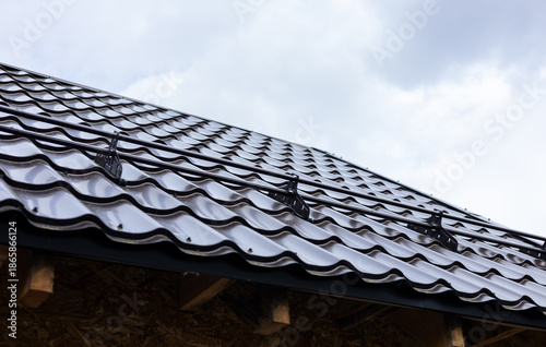 Closeup snow guard for safety in winter on house roof top covered with ceramic shingles. Tiled covering of building. Snow guards on the roof