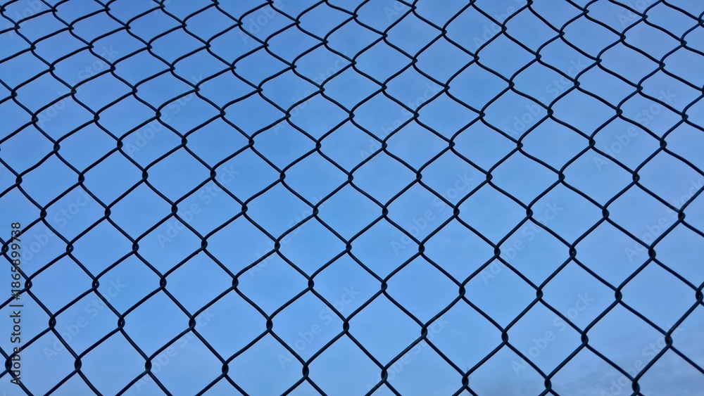 Fototapeta premium Perspective view of a metal wire mesh fence or chain link fence against a clear blue sky background. Concept of security, boundary, or restriction.