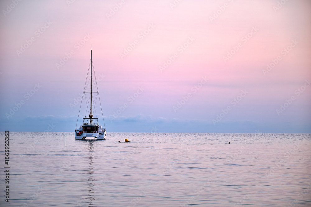Fototapeta premium Sailboat in calm water during sunset with swimmer nearby enjoying the ocean