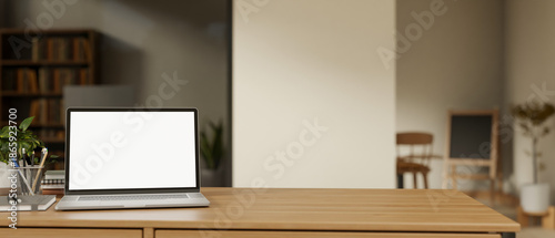 Blank screen laptop with book and pencil on wooden table across glass wall in a living room or cafe. © bongkarn