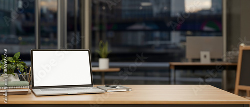 White screen laptop with book and pencil on wooden table across glass wall in office room at company
