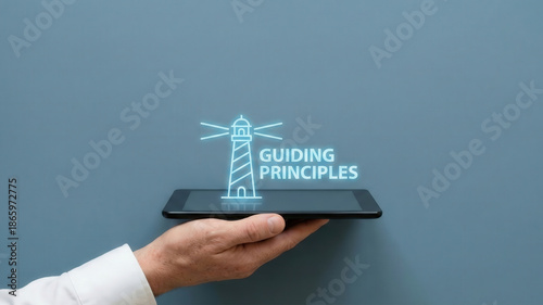 Business high level planning concept guiding principle lighthouse icon glows above digital tablet hand metaphor for corporate vision and leadership