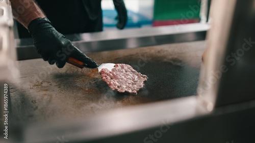 Foto Chef in black gloves cooking a smash burger patty on a hot grill in a dark kitch