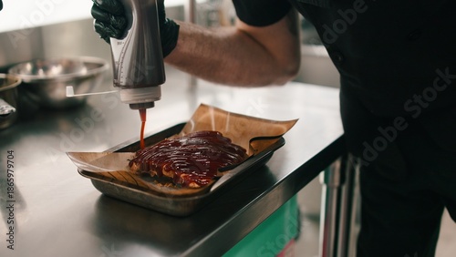 Принти на полотні Chef glazing ribs with bbq sauce using a squeeze bottle in dark kitchen workflow