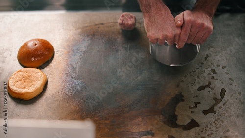 Chef hands smashing beef burger patty on hot griddle with toasted buns