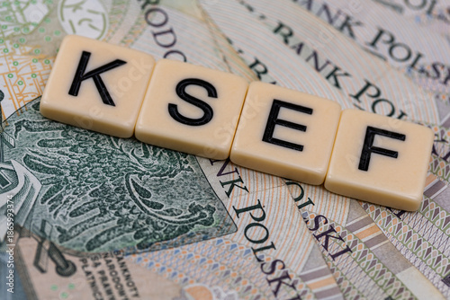 Blocks with the abbreviation KSEF, standing for National E-invoice System, are placed against a background of loosely spread Polish 100 PLN banknotes. The photo was taken under artificial lighting.