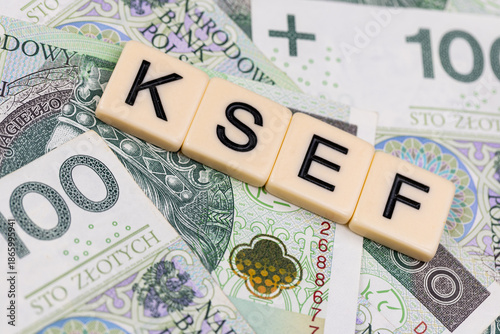 Blocks with the abbreviation KSEF, standing for National E-invoice System, are placed against a background of loosely spread Polish 100 PLN banknotes. The photo was taken under artificial lighting.